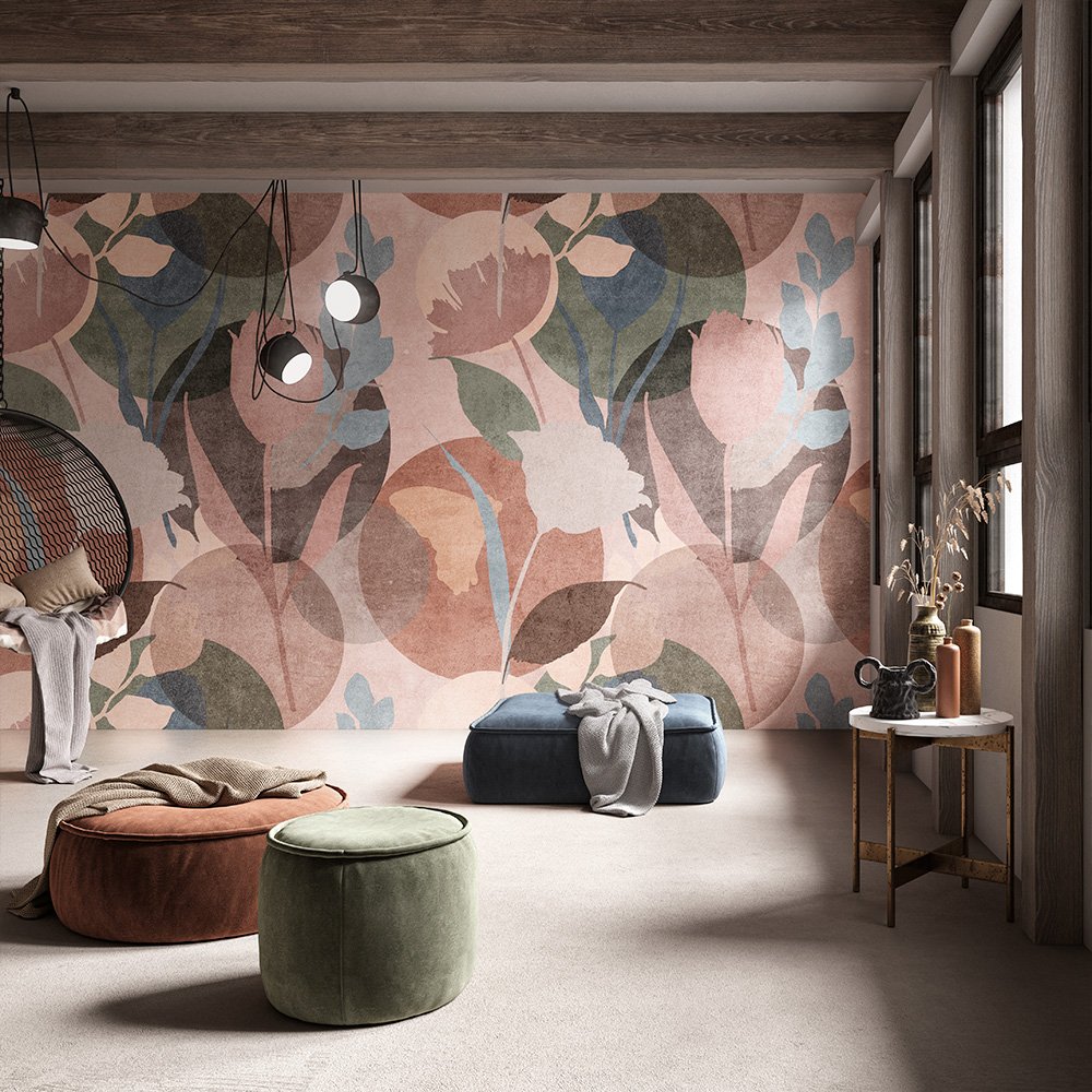 Pouf in velluto blu, verde e ruggine davanti a una parete a grandi foglie rosa