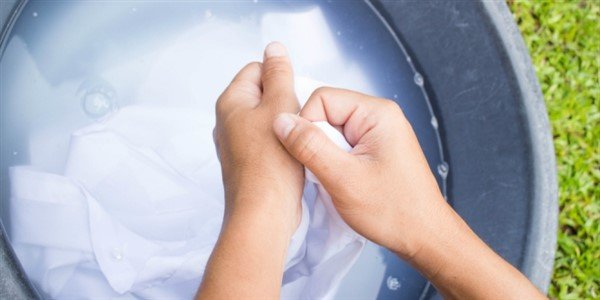 Mani che lavano un tessuto bianco in una bacinella d’acqua