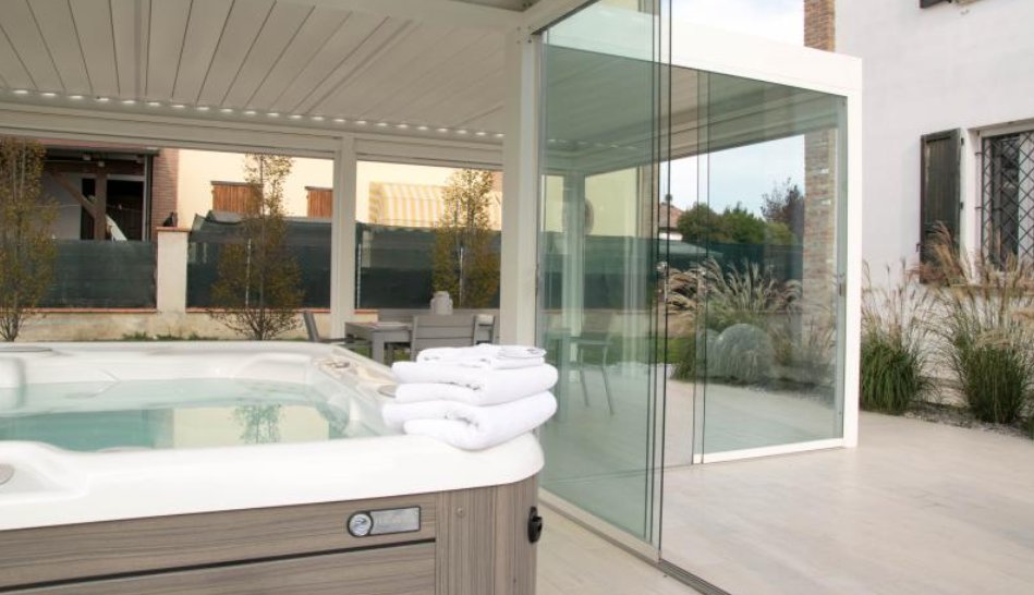 Pergola chiusa da ante in vetro con una vasca idromassaggio all’interno