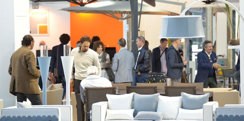 Visitatori tra divani, ombrelloni e lampade da esterno in uno stand di Sia Guest