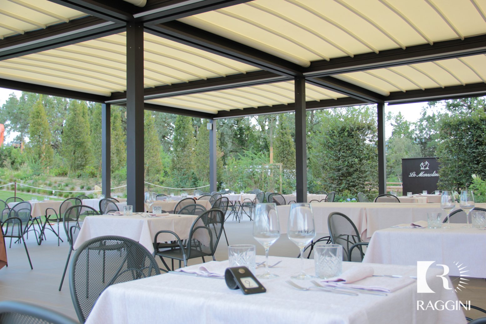 Sala ristorante all’aperto sotto una pergola con copertura in tessuto, tavoli apparecchiati e giardino sullo sfondo