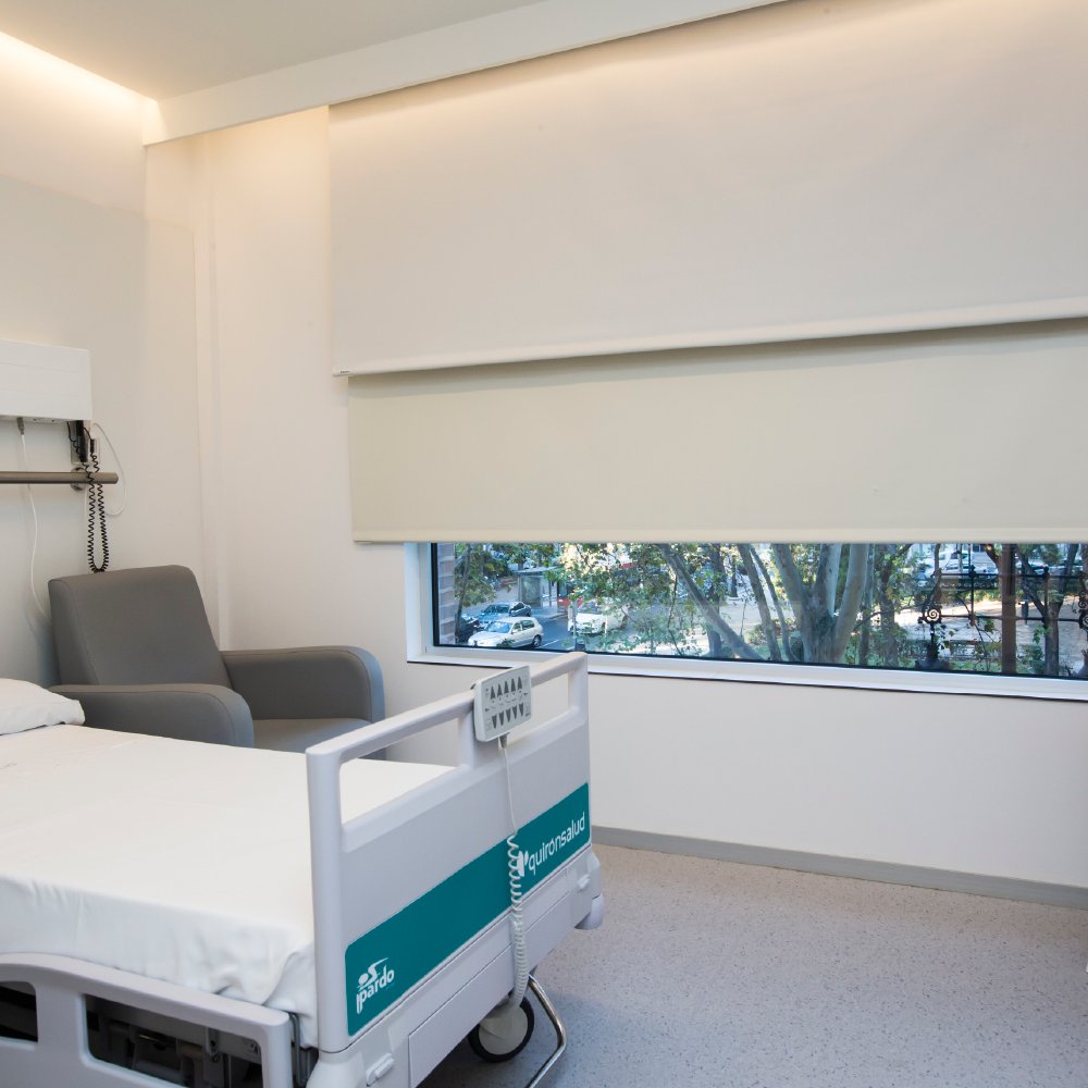 Stanza di degenza ospedaliera con tenda a rullo bianca abbassata sulla finestra