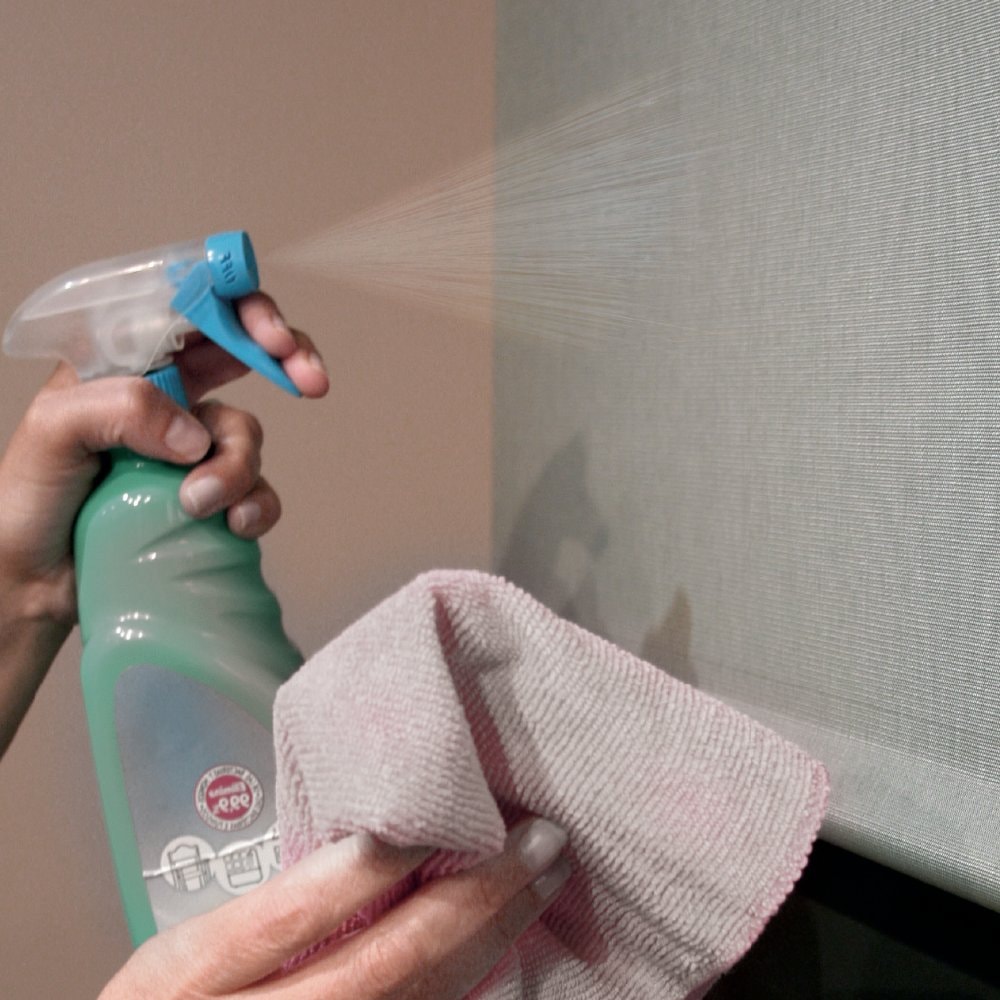 Mano che spruzza un disinfettante e pulisce con un panno una tenda a rullo