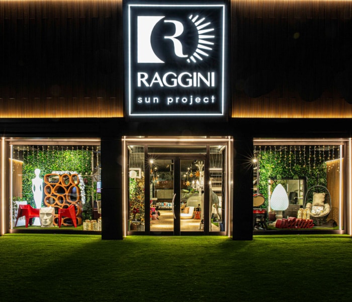 Facciata illuminata dello showroom Raggini Sun Project di sera, con le vetrine sull’arredo da esterno