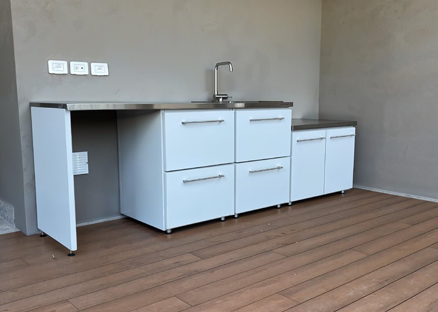 Cucina da esterno bianca con lavello e cassetti sotto un portico con pavimento in legno