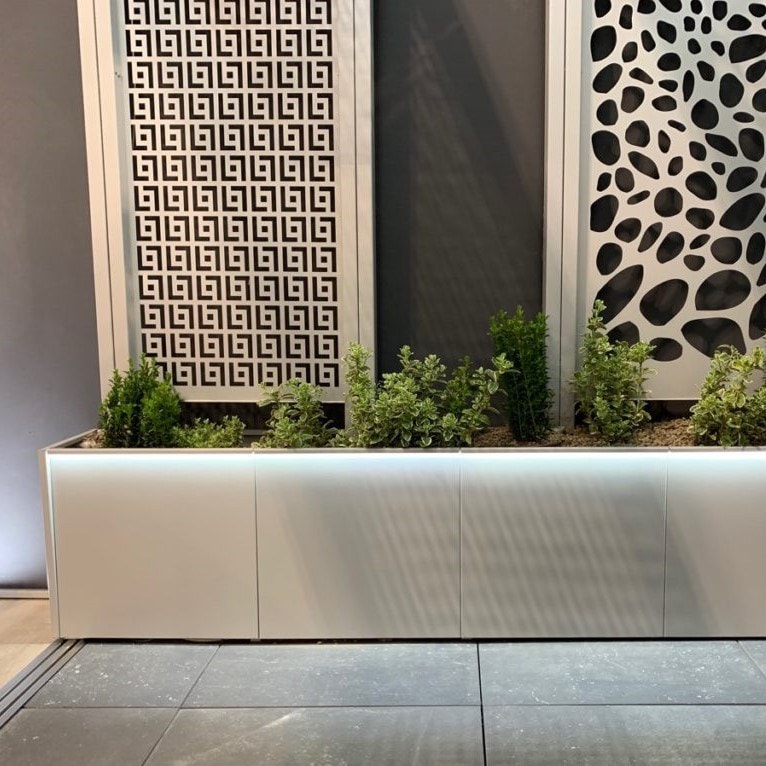 Fioriera lunga con strip LED alla base, davanti a pannelli decorativi traforati