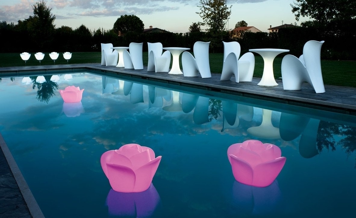 Sedute bianche a bordo piscina e lampade a forma di rosa che galleggiano nell’acqua