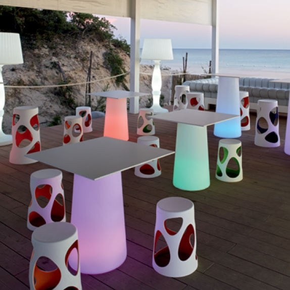 Sgabelli bianchi traforati e tavoli luminosi su una terrazza in riva al mare