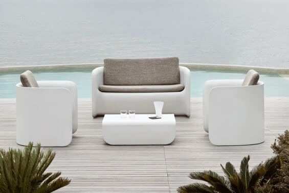 Salotto bianco con divano, poltrone e tavolino su una terrazza in legno a bordo piscina
