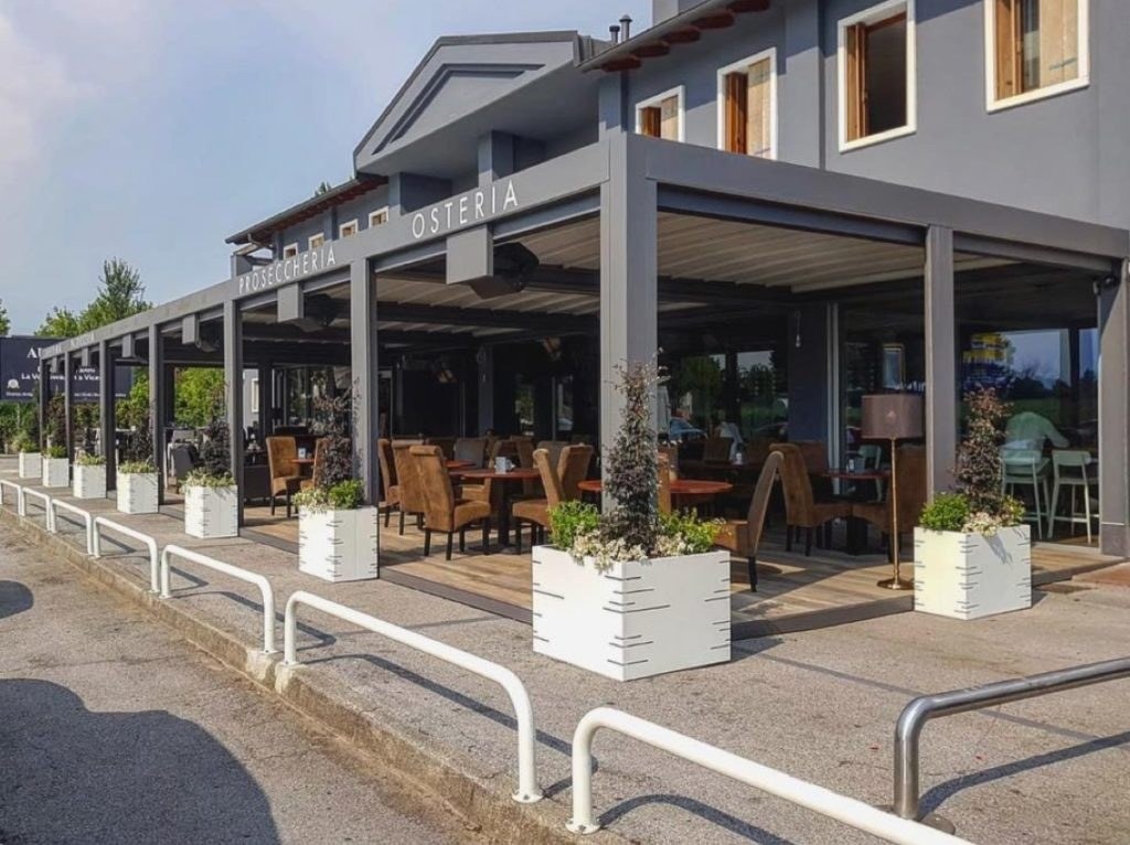 Pergola antracite davanti a un’osteria, con fioriere Pergo Potter bianche alle colonne