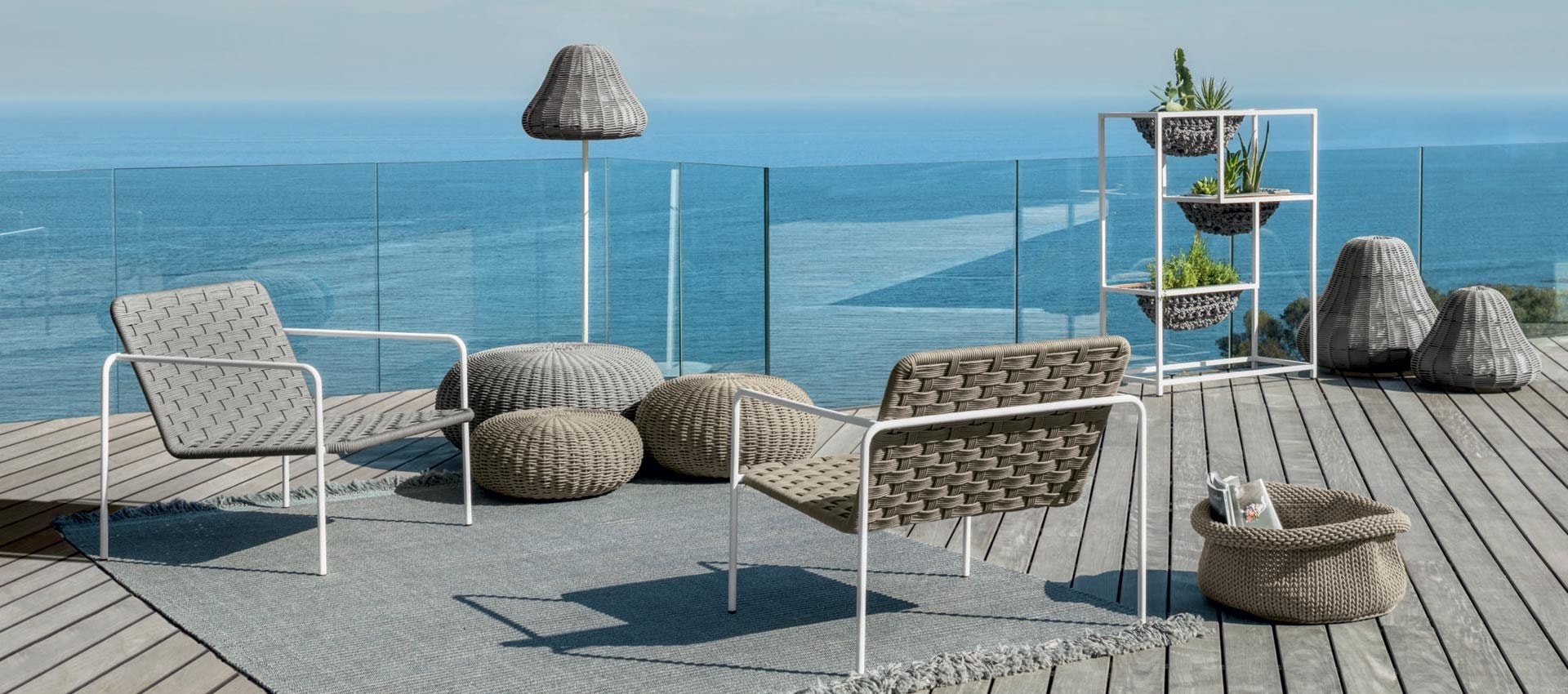 Poltrone in corda e pouf intrecciati su una terrazza in legno vista mare