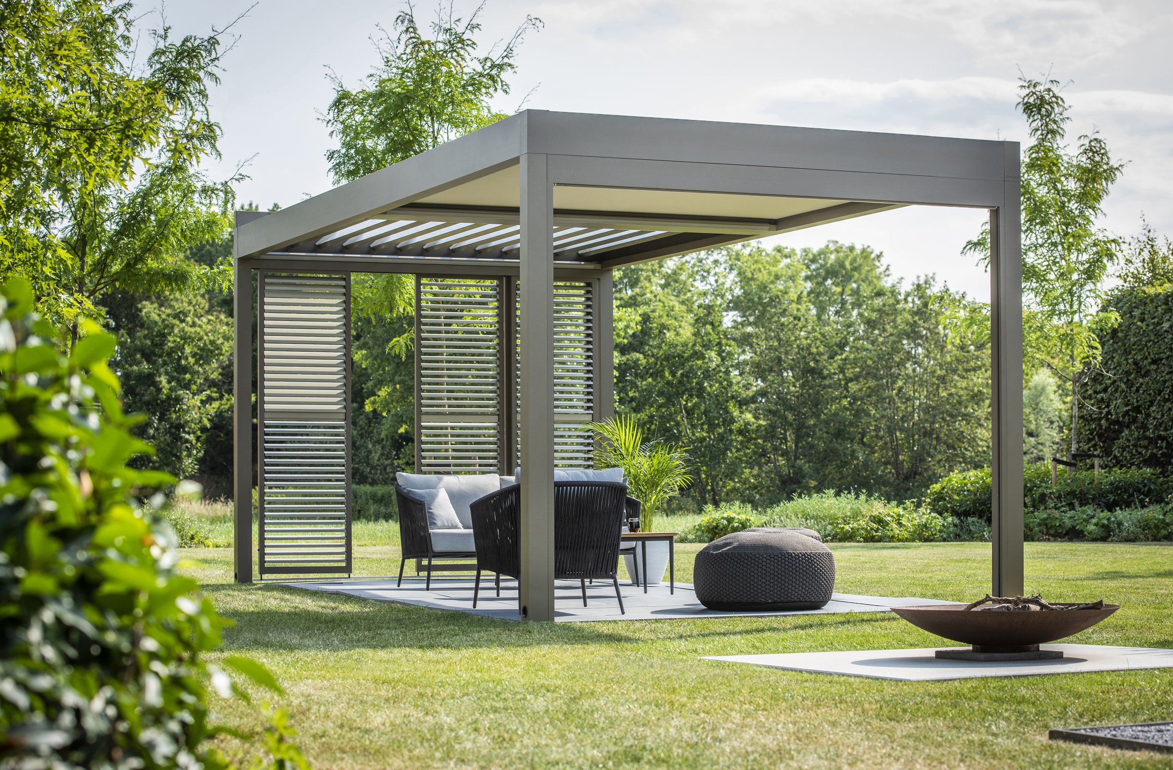 Pergola Algarve autoportante su un prato, con salotto e pannello laterale a lamelle