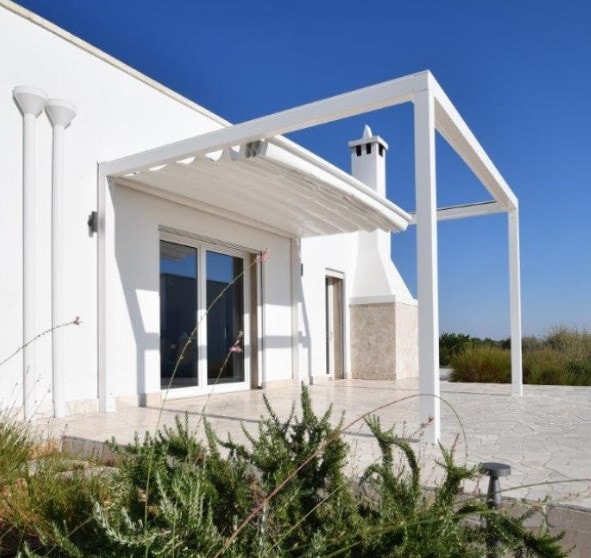 Pergola Round K bianca accanto a una casa, vista di lato