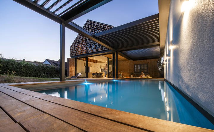 Pergola Skye accanto a una piscina illuminata, all’imbrunire