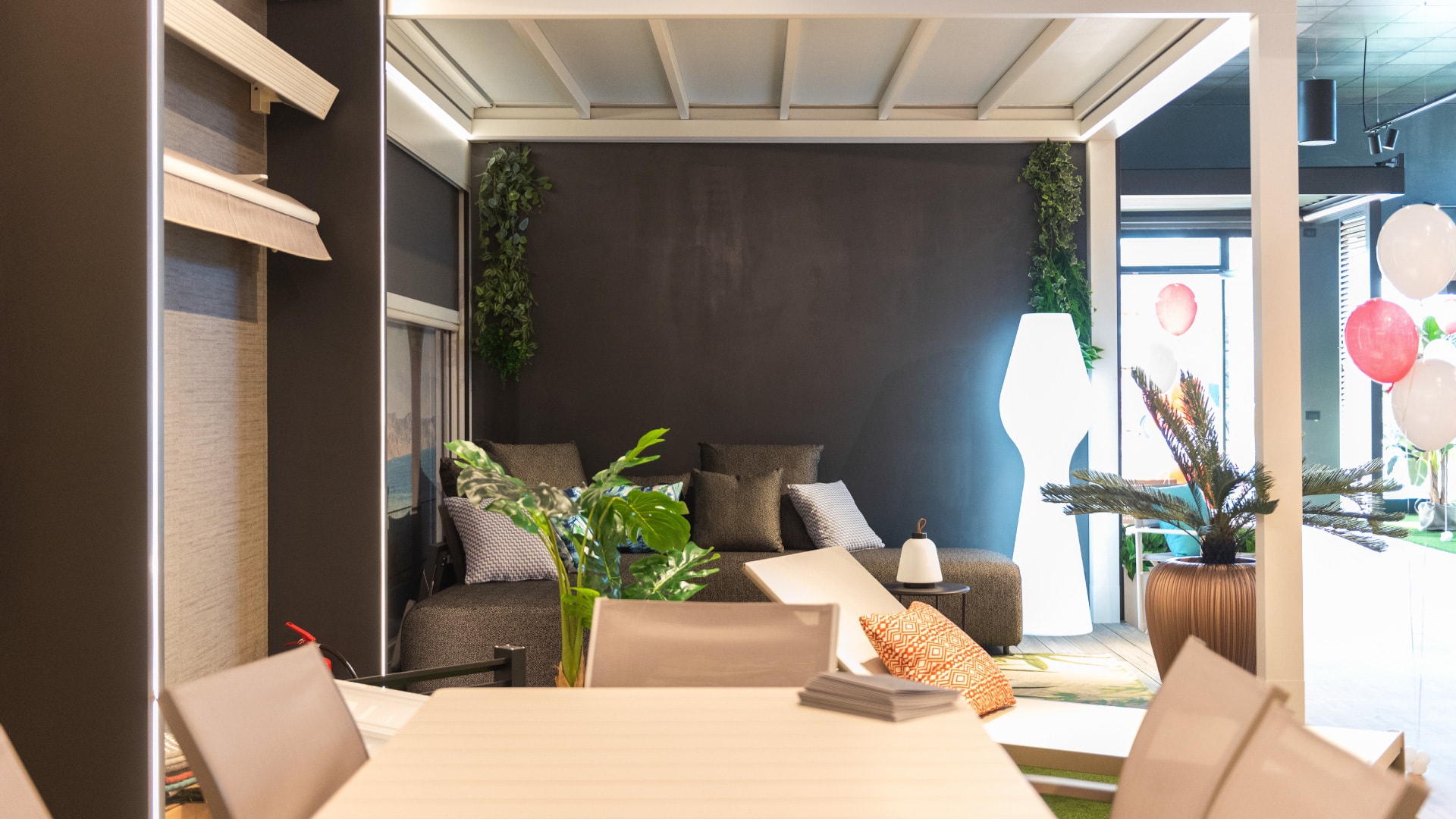 Pergola bianca allestita con divano, piante e lampada da terra all’interno dello showroom Sun Project