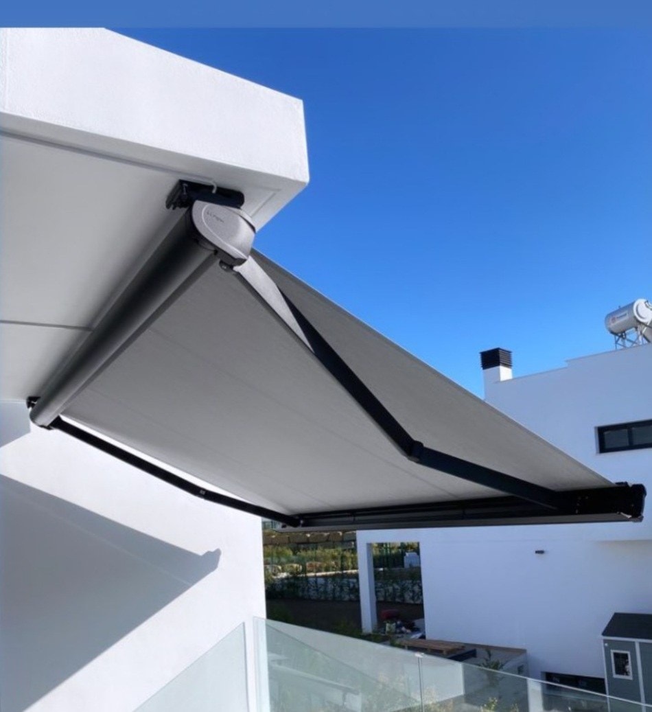 Tenda Elettra grigia con bracci scuri su una casa bianca, vista dal basso