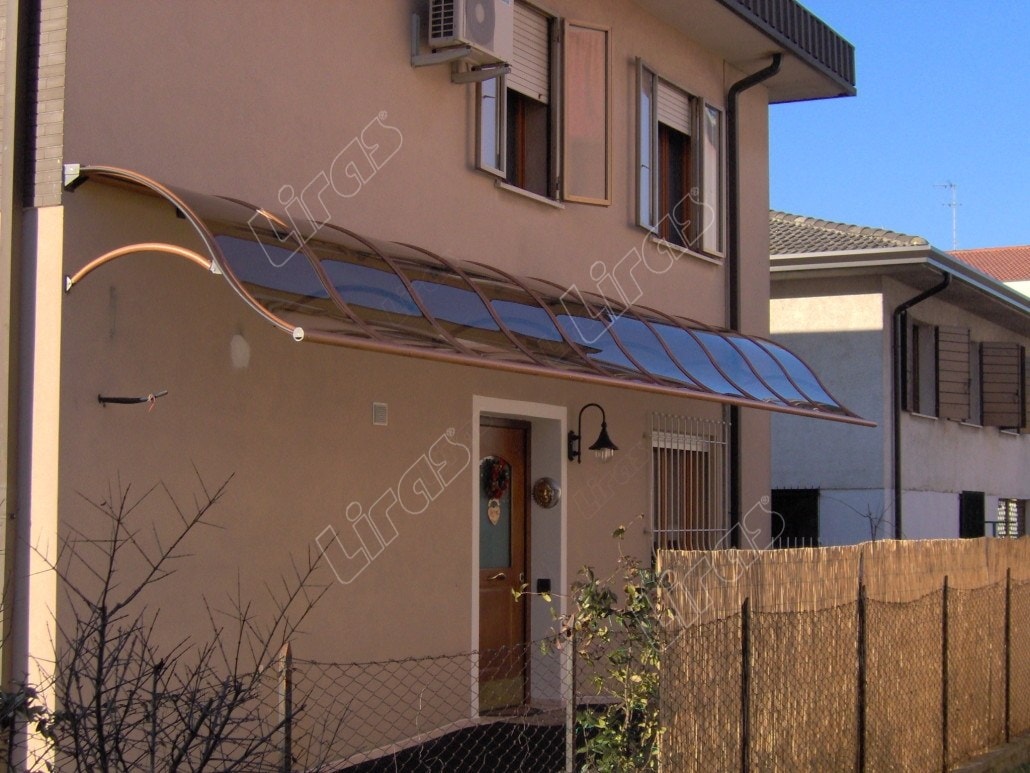 Lunga pensilina con archi ondulati color rame sulla facciata di una casa