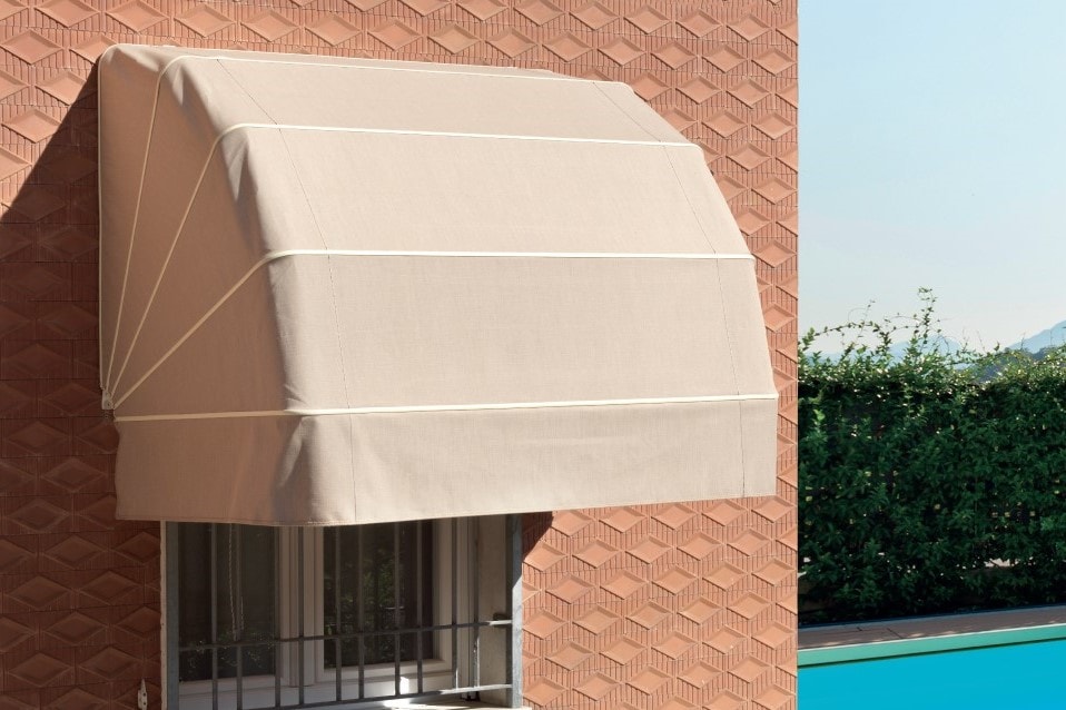 Tenda a cappottina beige sopra una finestra, su una parete in mattoni