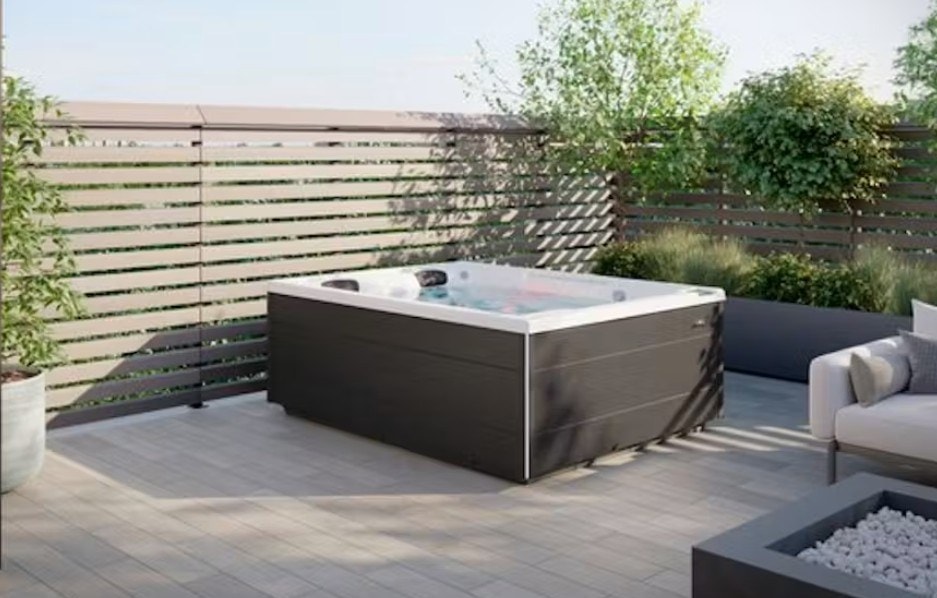 Spa con pannelli scuri su una terrazza con divani e staccionata in legno