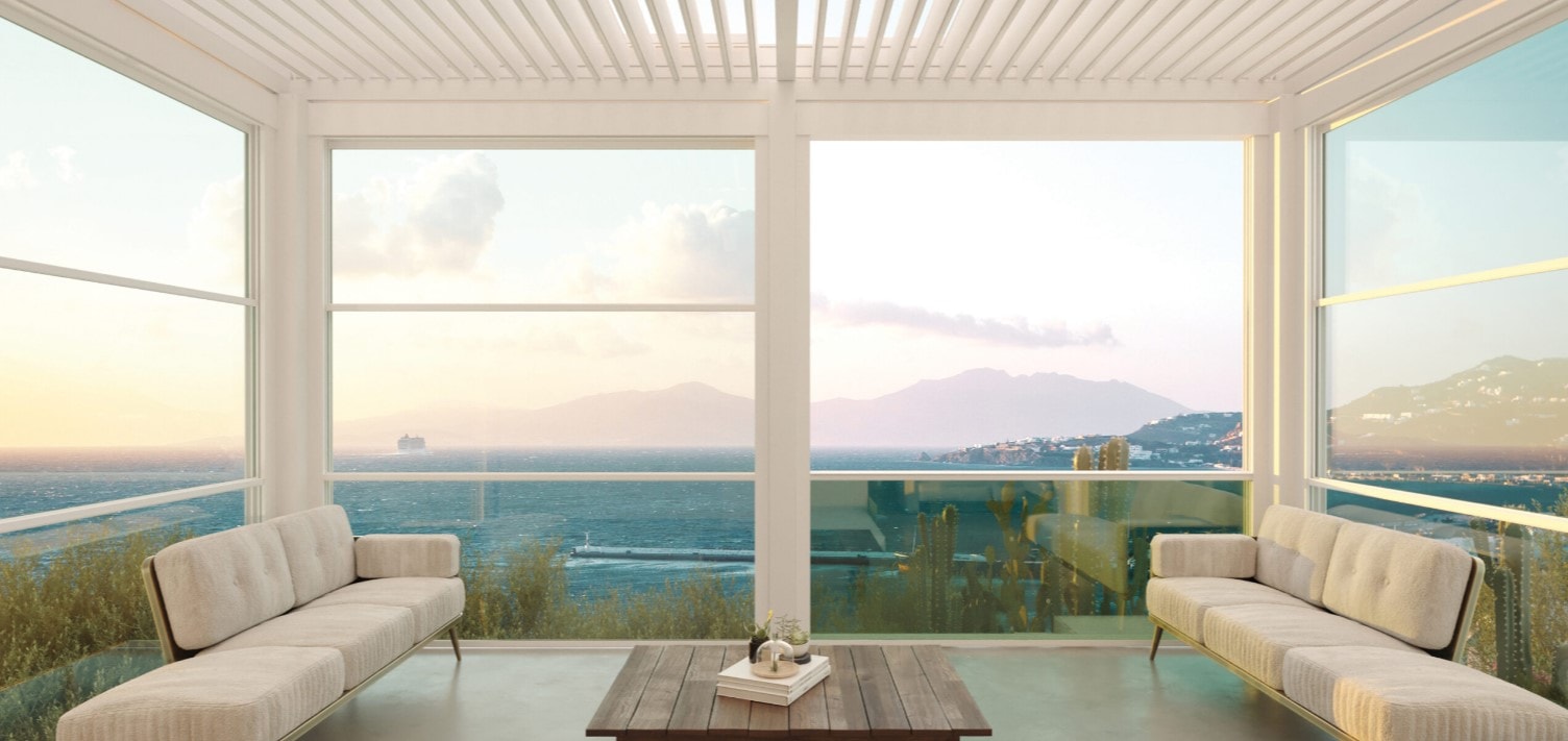 Salotto vista mare sotto una pergola a lamelle, chiuso da vetrate saliscendi