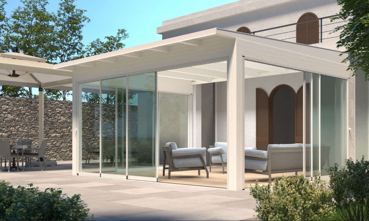 Pergola bianca chiusa da vetrate scorrevoli Slide Glass, con un salotto, accanto a una villa