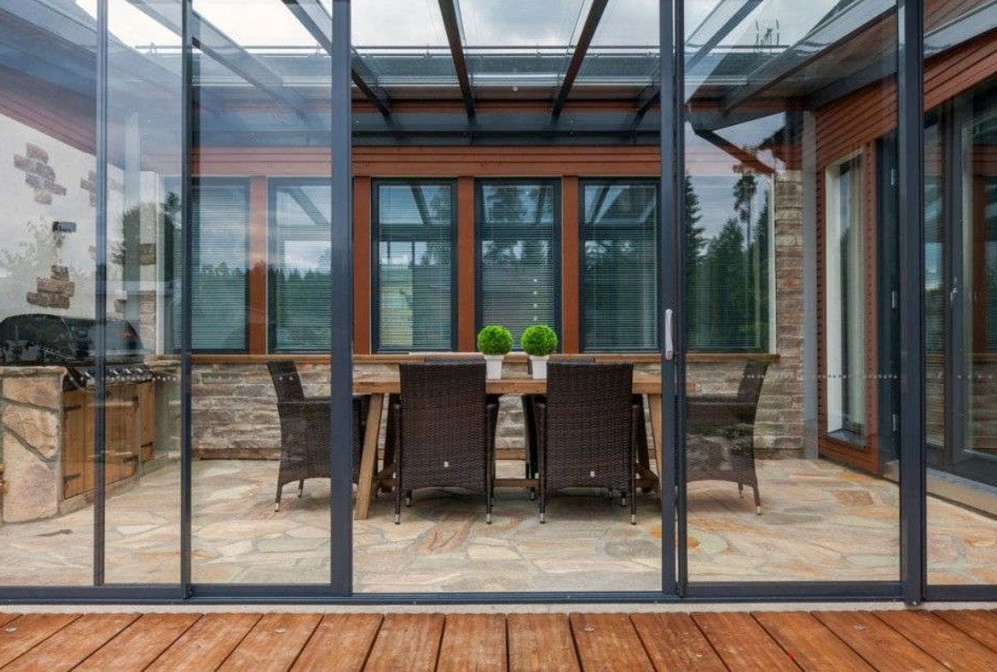 Patio con tetto in vetro chiuso da vetrate scorrevoli, con tavolo da pranzo e cucina in pietra
