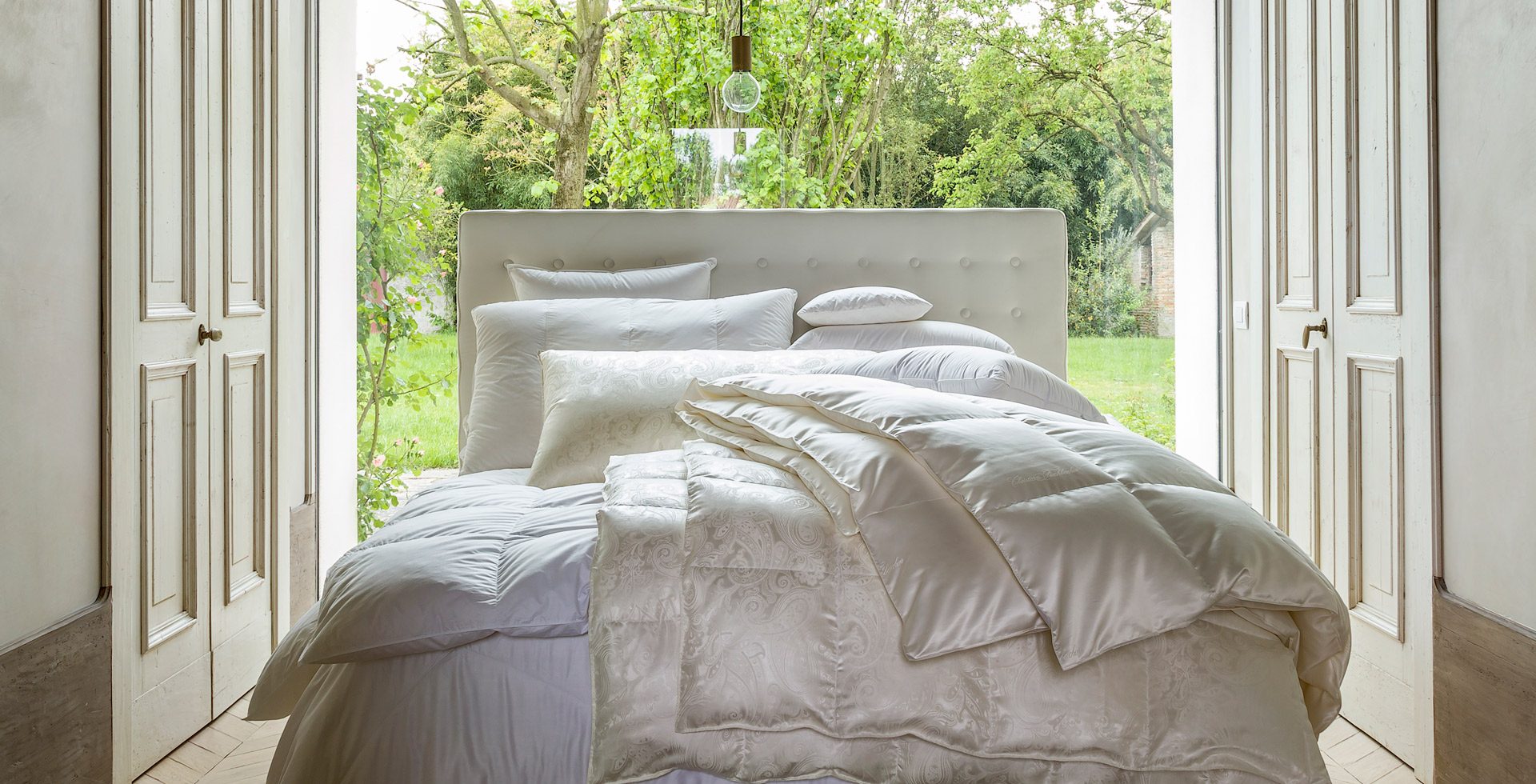 Piumino bianco su un letto davanti a una vetrata affacciata sul verde