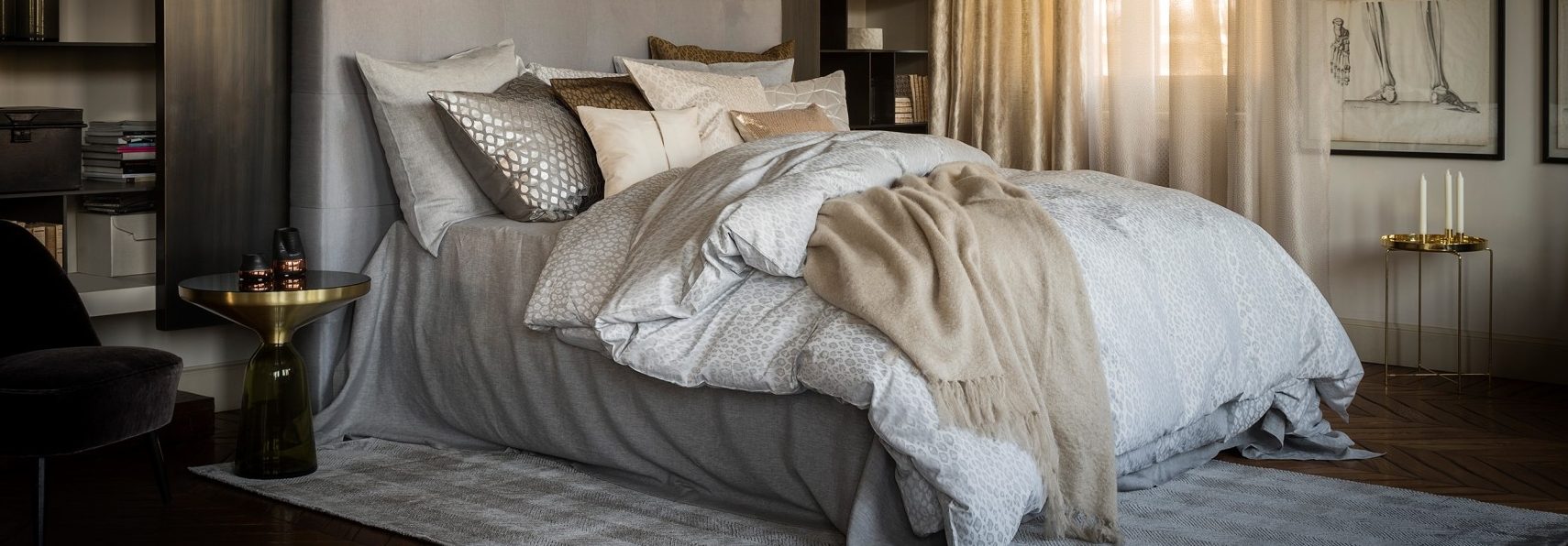 Letto matrimoniale con biancheria chiara e cuscini ricamati, in una camera scura