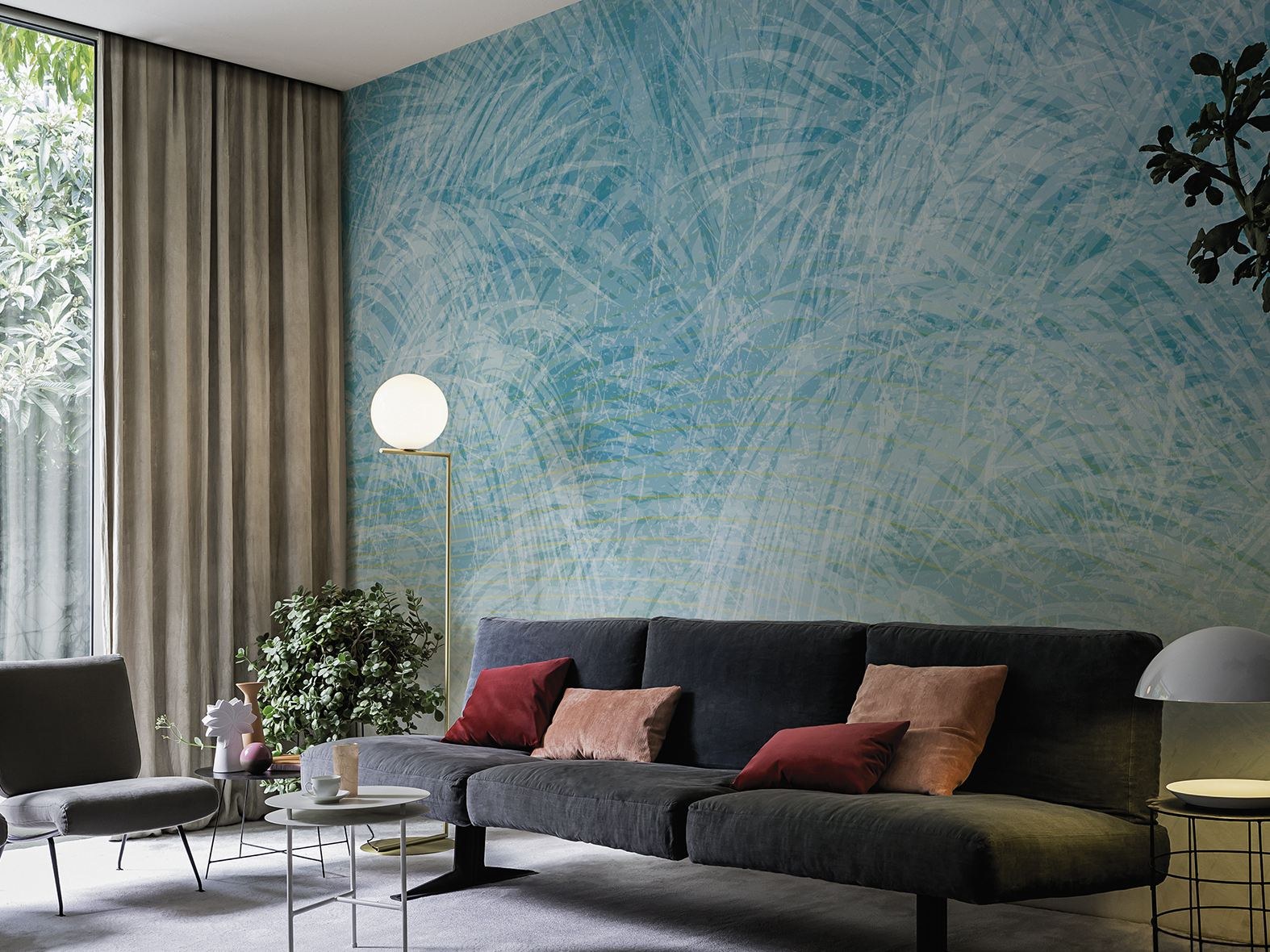 Soggiorno con divano grigio davanti a una parete azzurra decorata a foglie