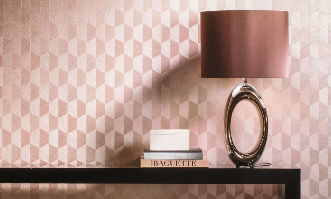 Consolle nera con lampada da tavolo e libri davanti a una parete rosa a losanghe