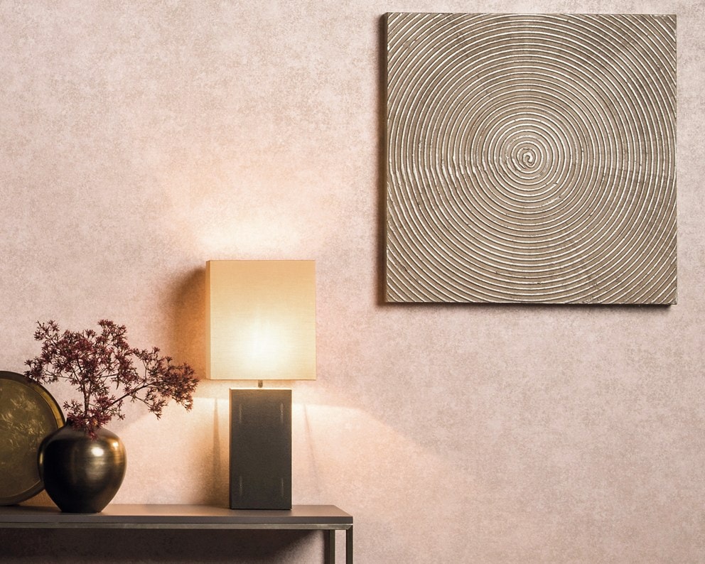 Mobile basso con lampada, vasi e un quadro a cerchi concentrici su una parete rosa