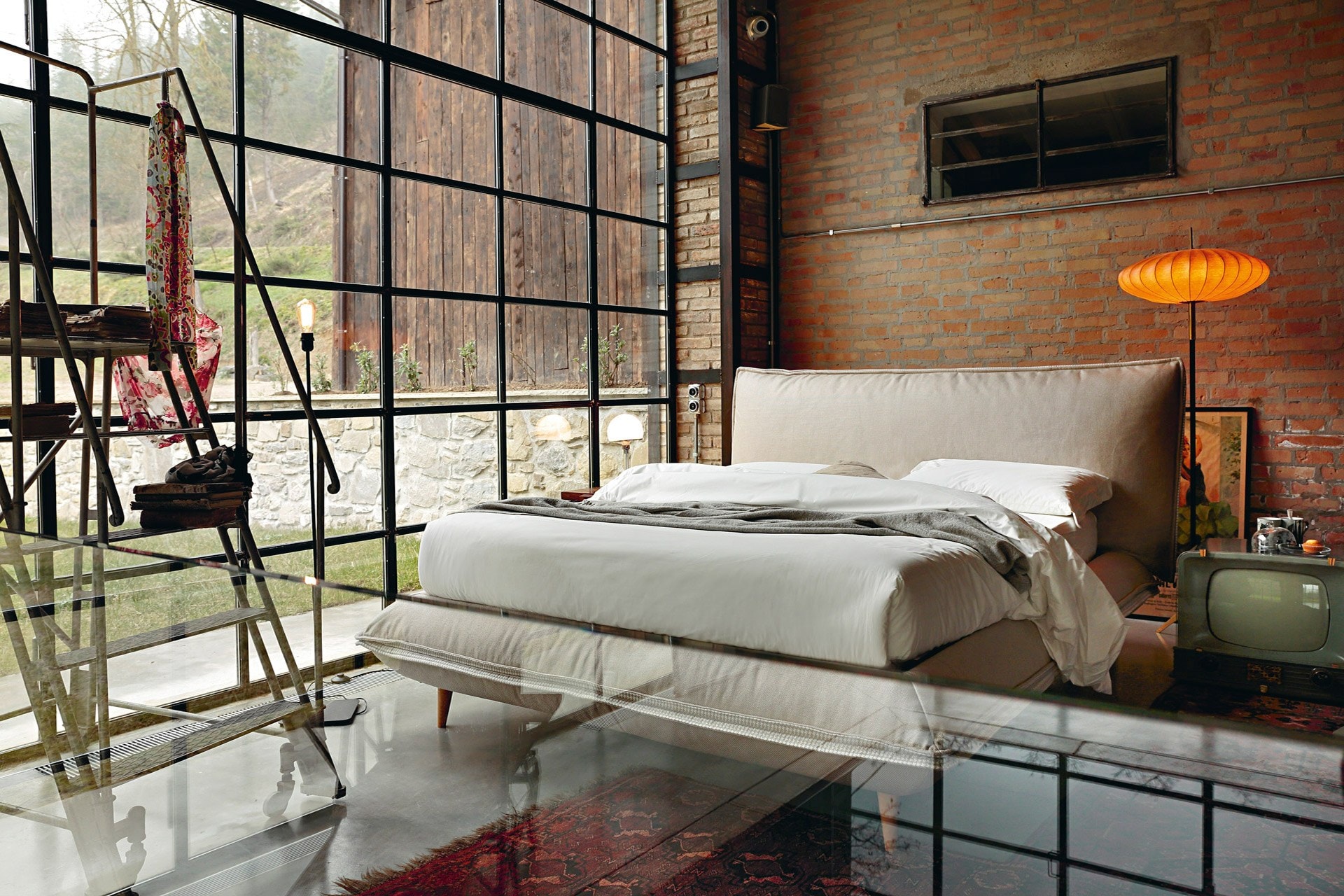 Letto imbottito in un loft con muri in mattoni e grandi vetrate