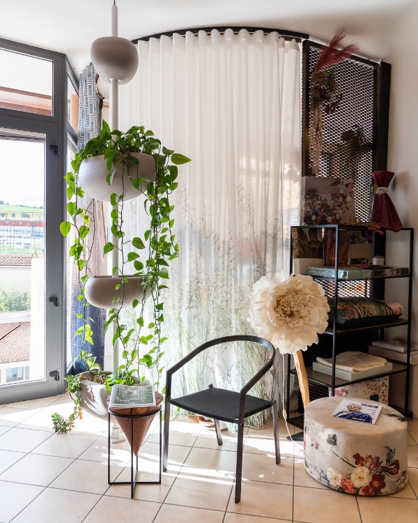 Angolo dello showroom con tenda bianca a motivi vegetali, piante sospese e campionari di tessuti