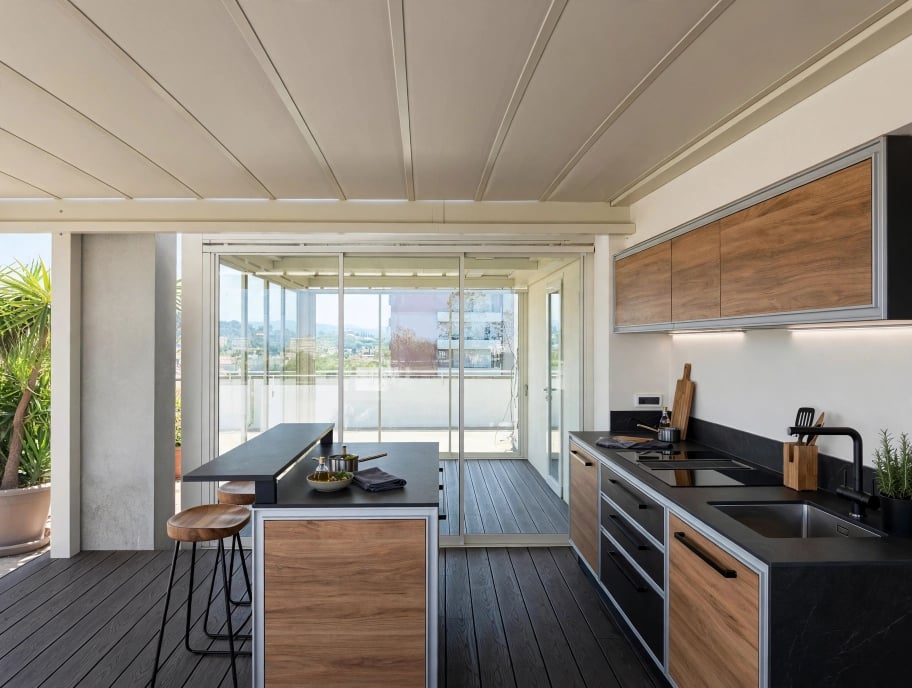 Cucina da esterno sotto una pergola chiusa da vetrate panoramiche