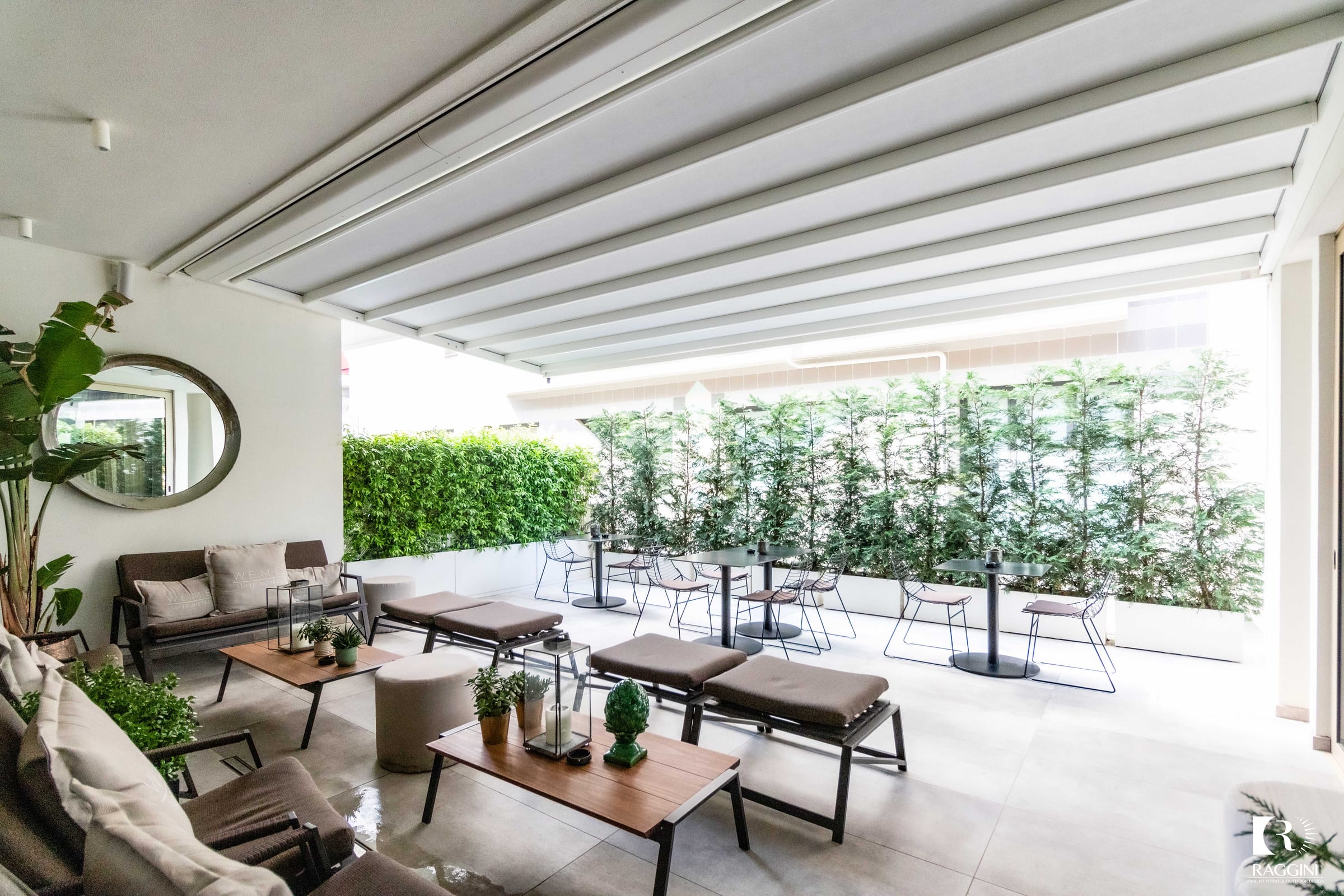 Terrazza chiusa da vetrate panoramiche, con salotto e tavolo da pranzo affacciati sul verde