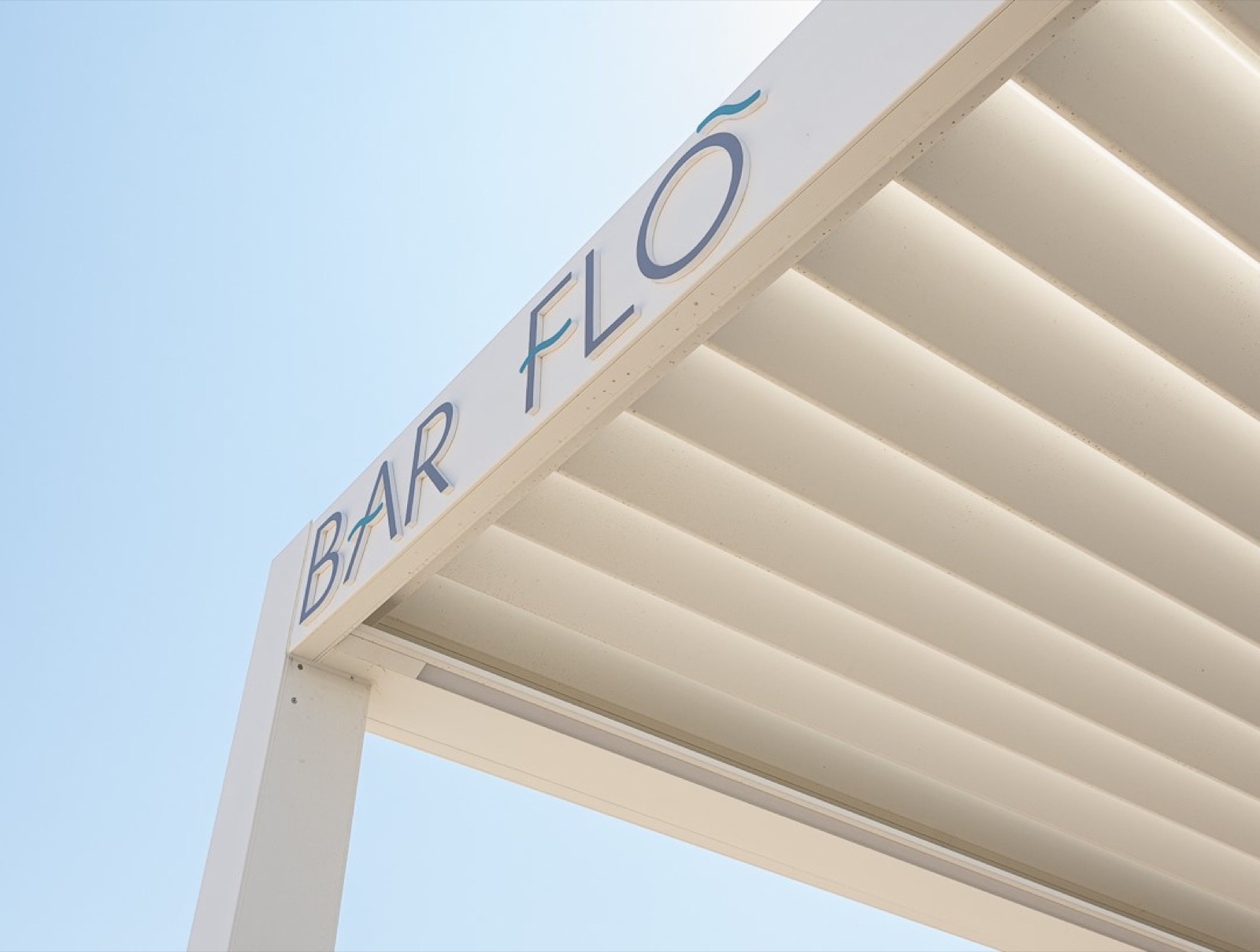 Pergola bioclimatica bianca Zefiro con la scritta Bar Flo, vista dal basso