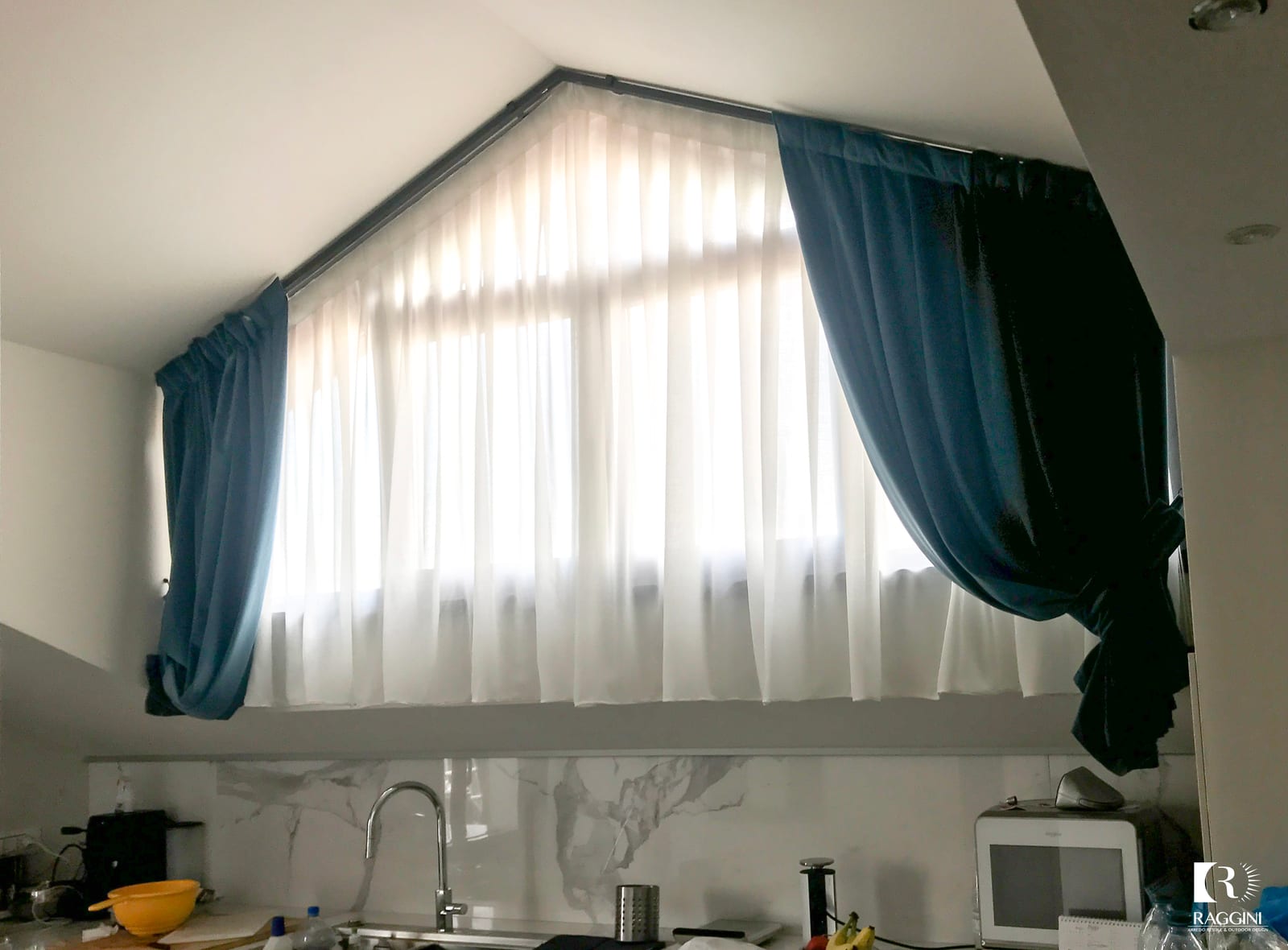Soggiorno dell'attico di Casa M+D con doppie tende in velluto ottanio lungo il soffitto spiovente