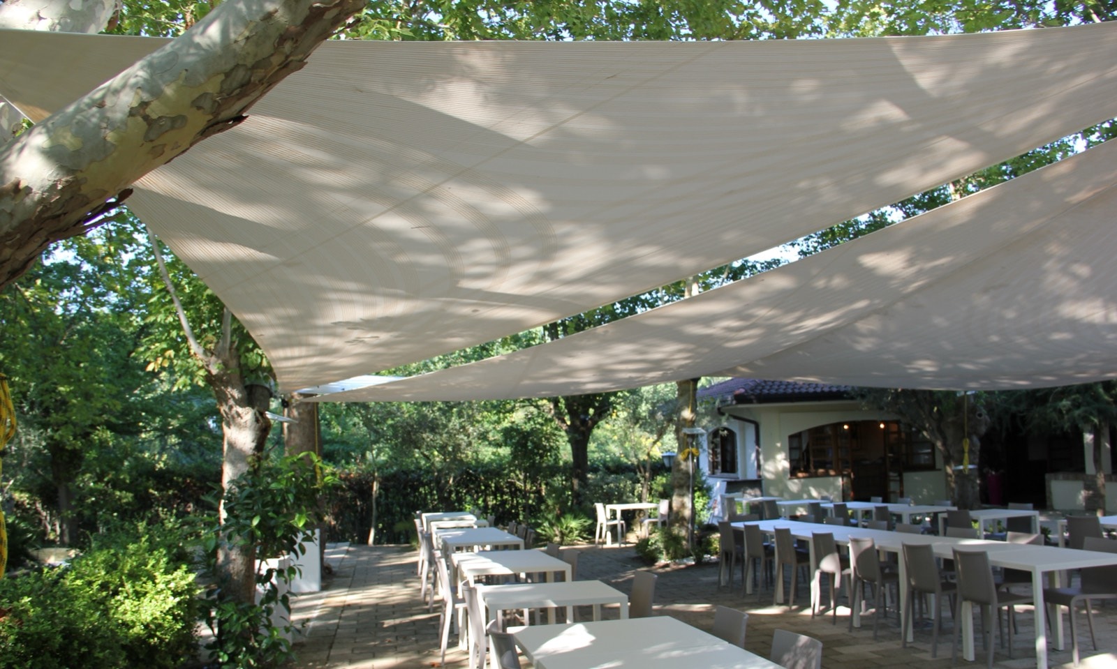 Vele ombreggianti tese fra gli alberi sopra i tavoli del giardino de La Vecchia Fonte
