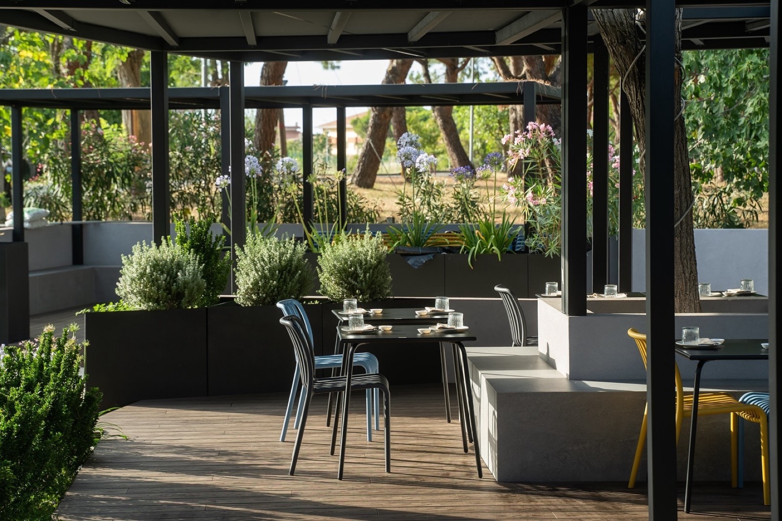 Dehors del ristorante Mana Sushi sotto una pergola scura, con divanetti e fioriere