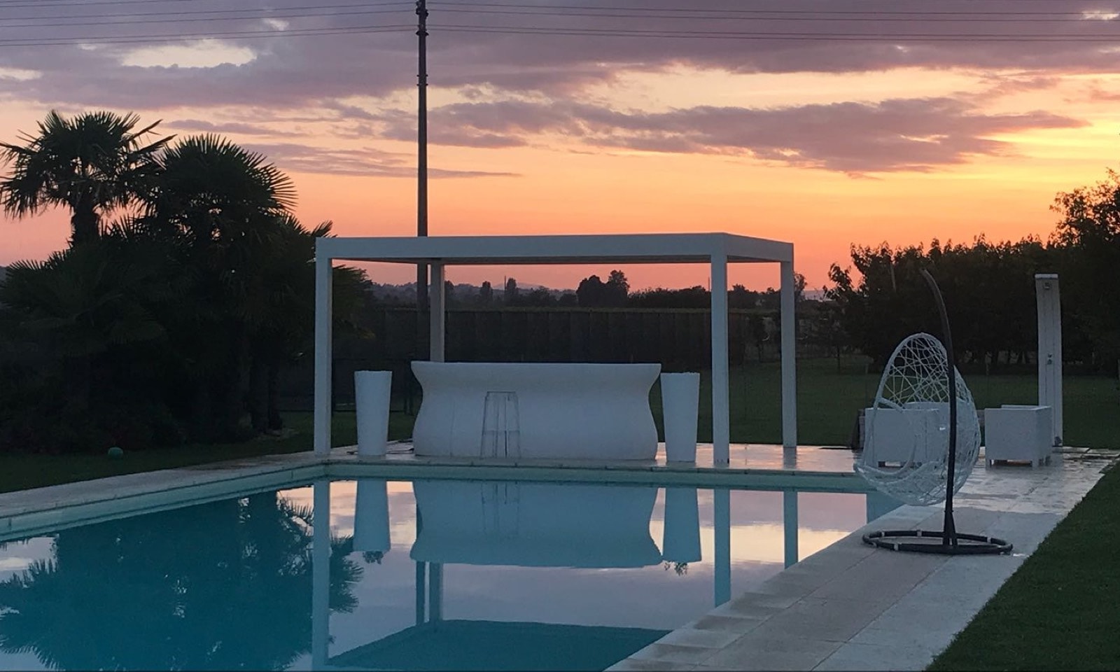 Pergola bianca a lamelle a bordo piscina al tramonto