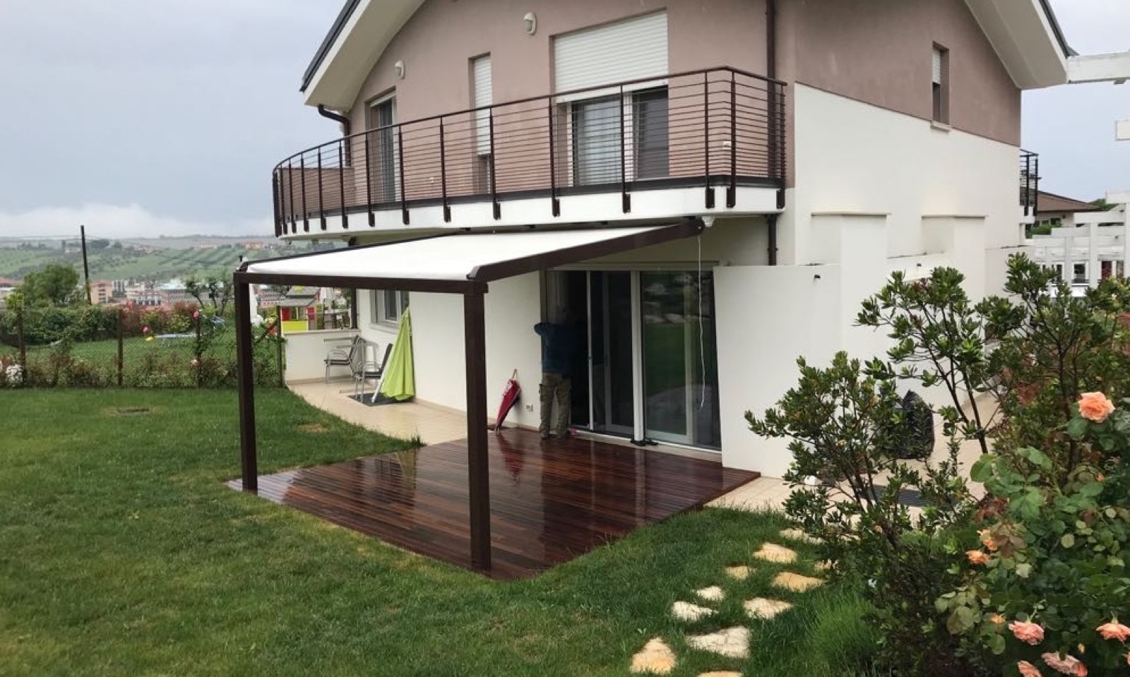 Pergola marrone con telo avvolgibile chiaro sopra una pedana in legno in giardino