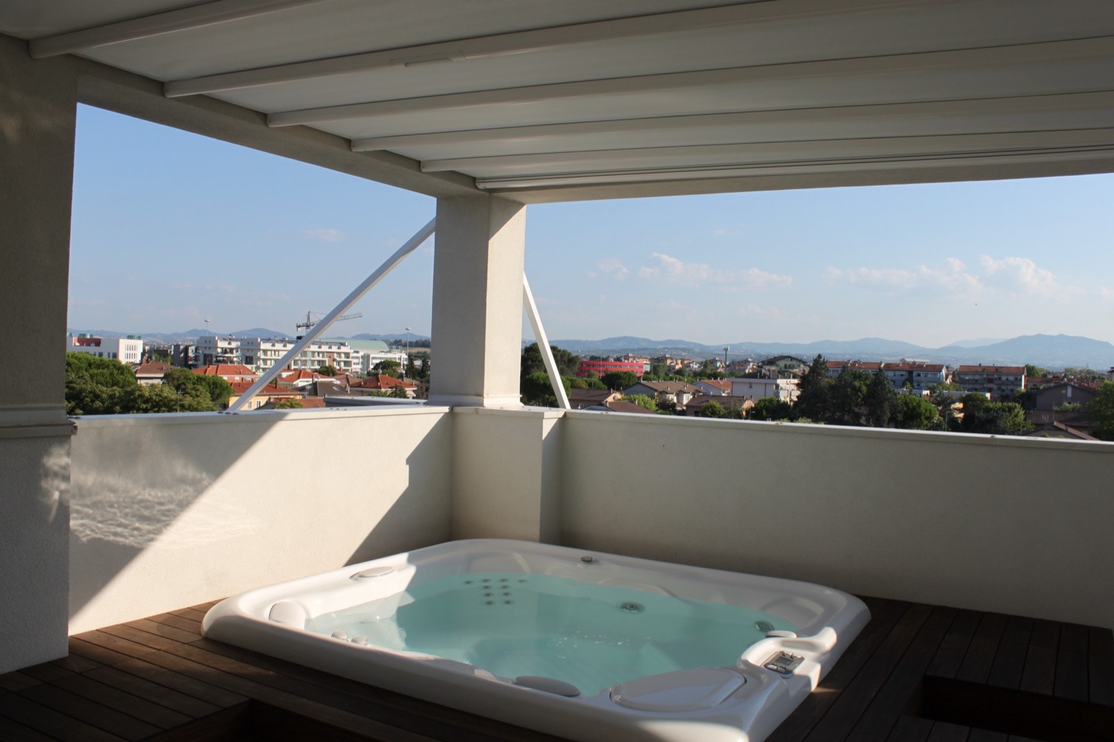 Pergotenda bianca sopra una mini SPA incassata in una pedana in legno sul balcone