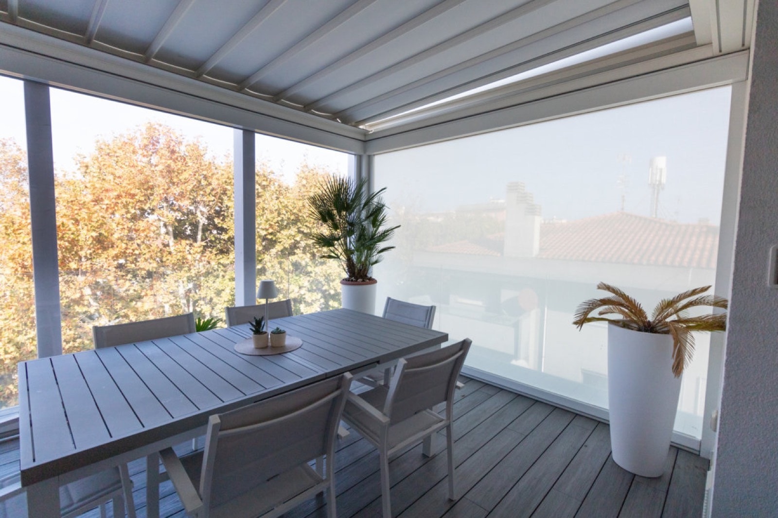 Pergola bianca con tende laterali screen sul terrazzo, con tavolo da pranzo