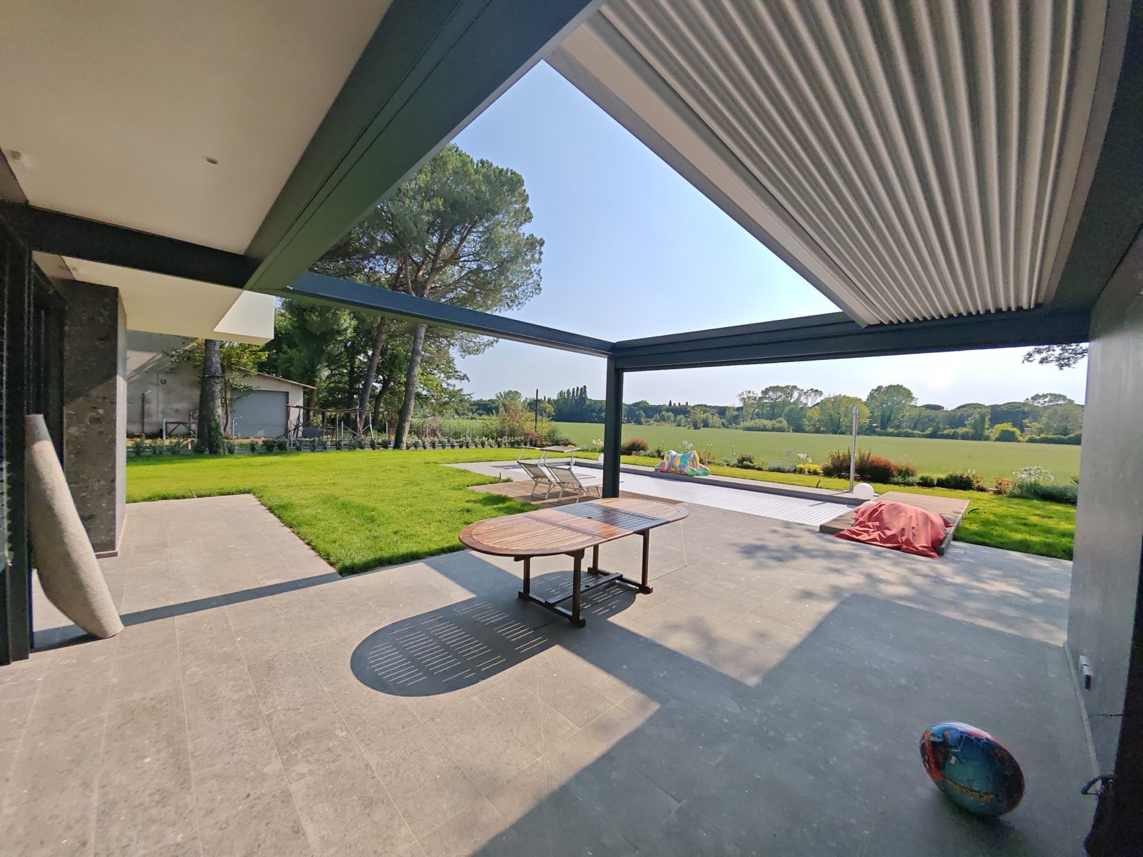 Pergola Blooming grigio antracite con telo retrattile sul patio di una villa, affacciata sul giardino