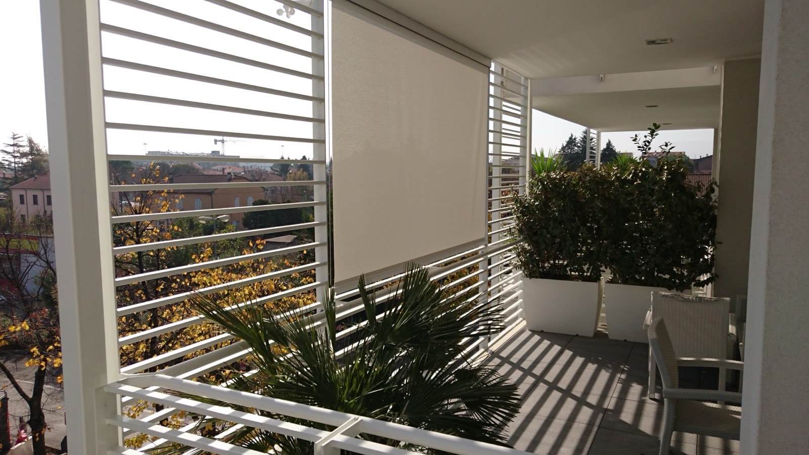 Tenda a caduta abbassata su un balcone con parapetto bianco e fioriere
