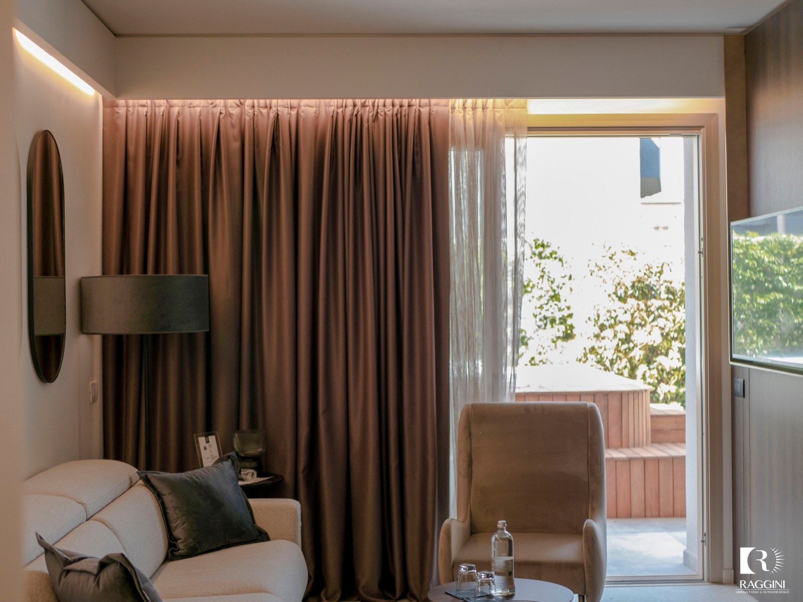 Poltrona color sabbia e divano chiaro davanti a tende color moka, in una suite