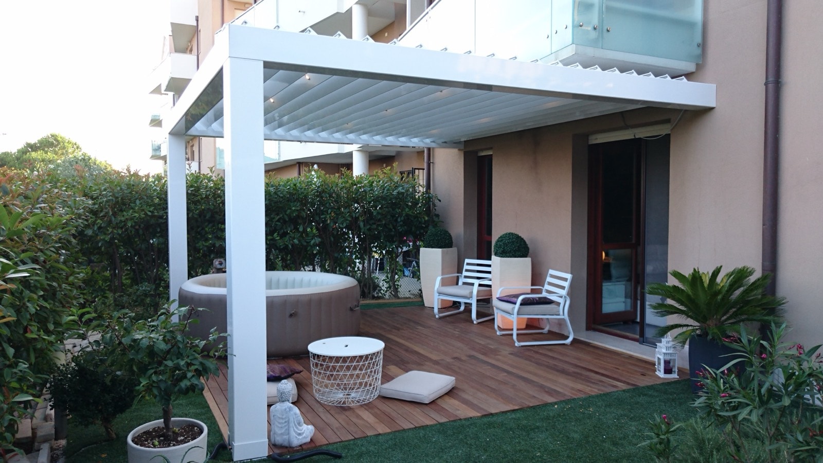 Pergola bioclimatica bianca su pedana in legno con vasca idromassaggio in giardino