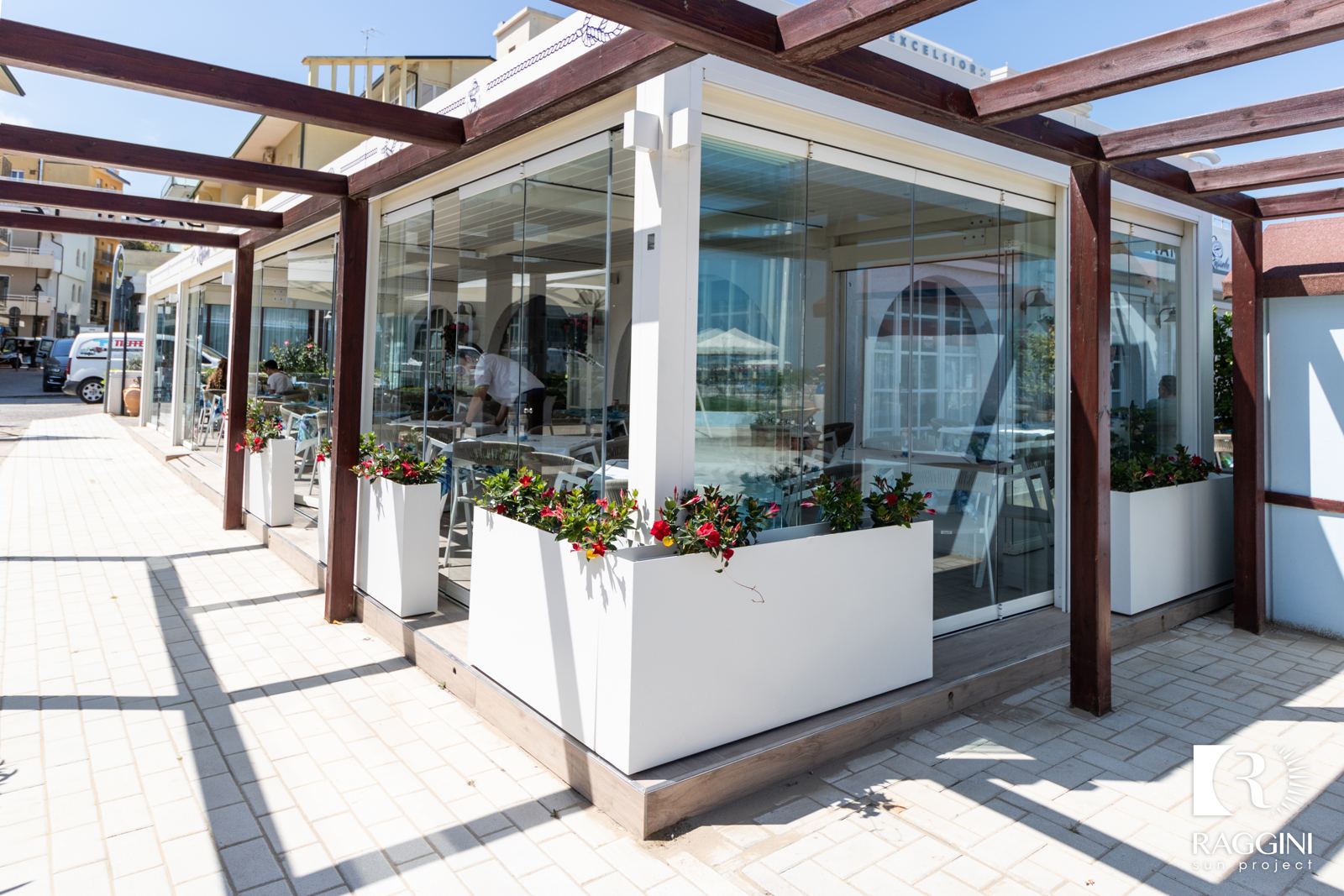 Dehors di un ristorante sotto una pergola bioclimatica bianca, chiuso da vetrate
